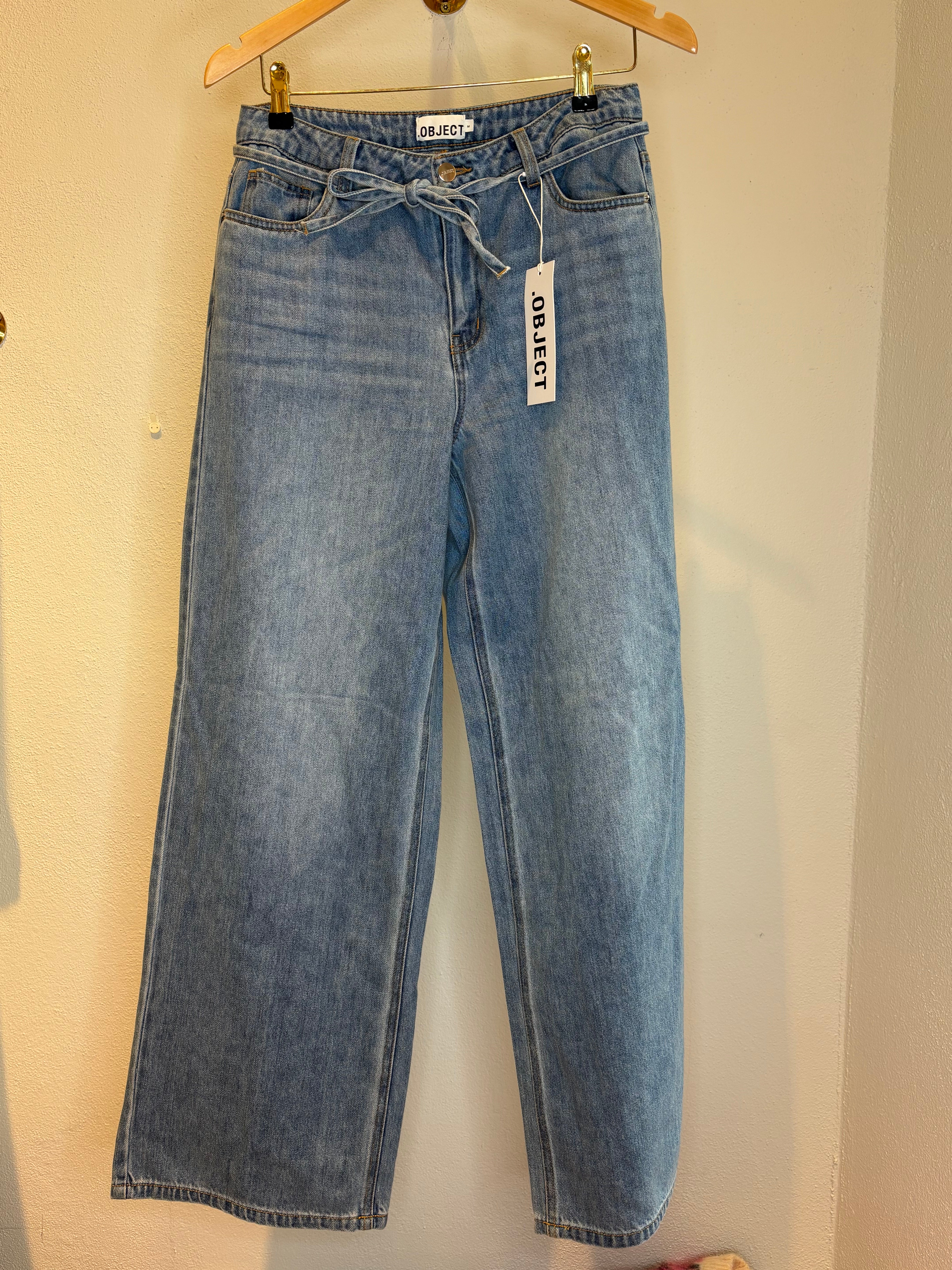 Objrosie Wide Jeans Light Blue Denim. Blåa jeans med snörning hängandes på en galge.