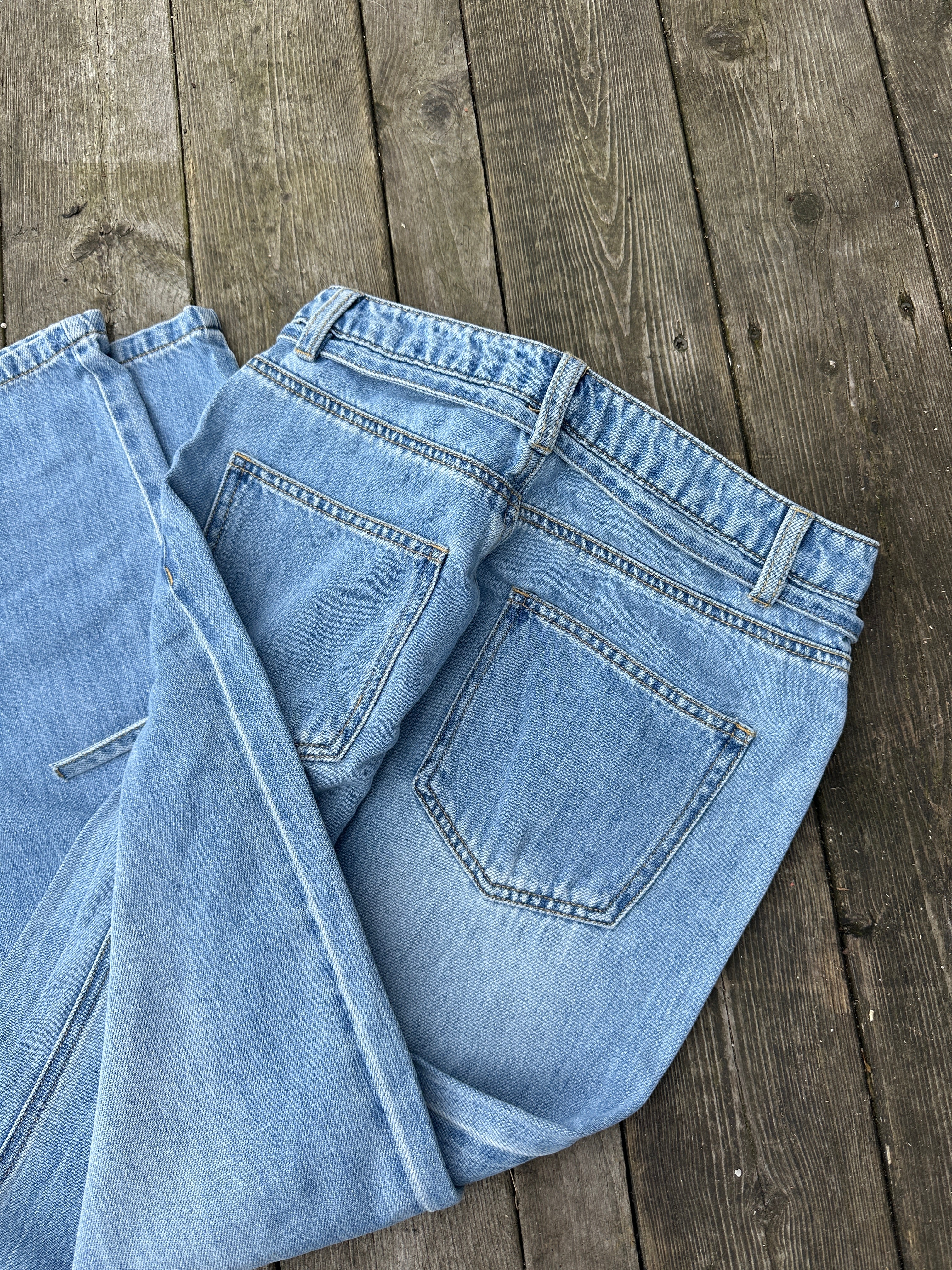 Objrosie Wide Jeans Light Blue Denim. Blåa jeans med snörning liggandes på en brygga.