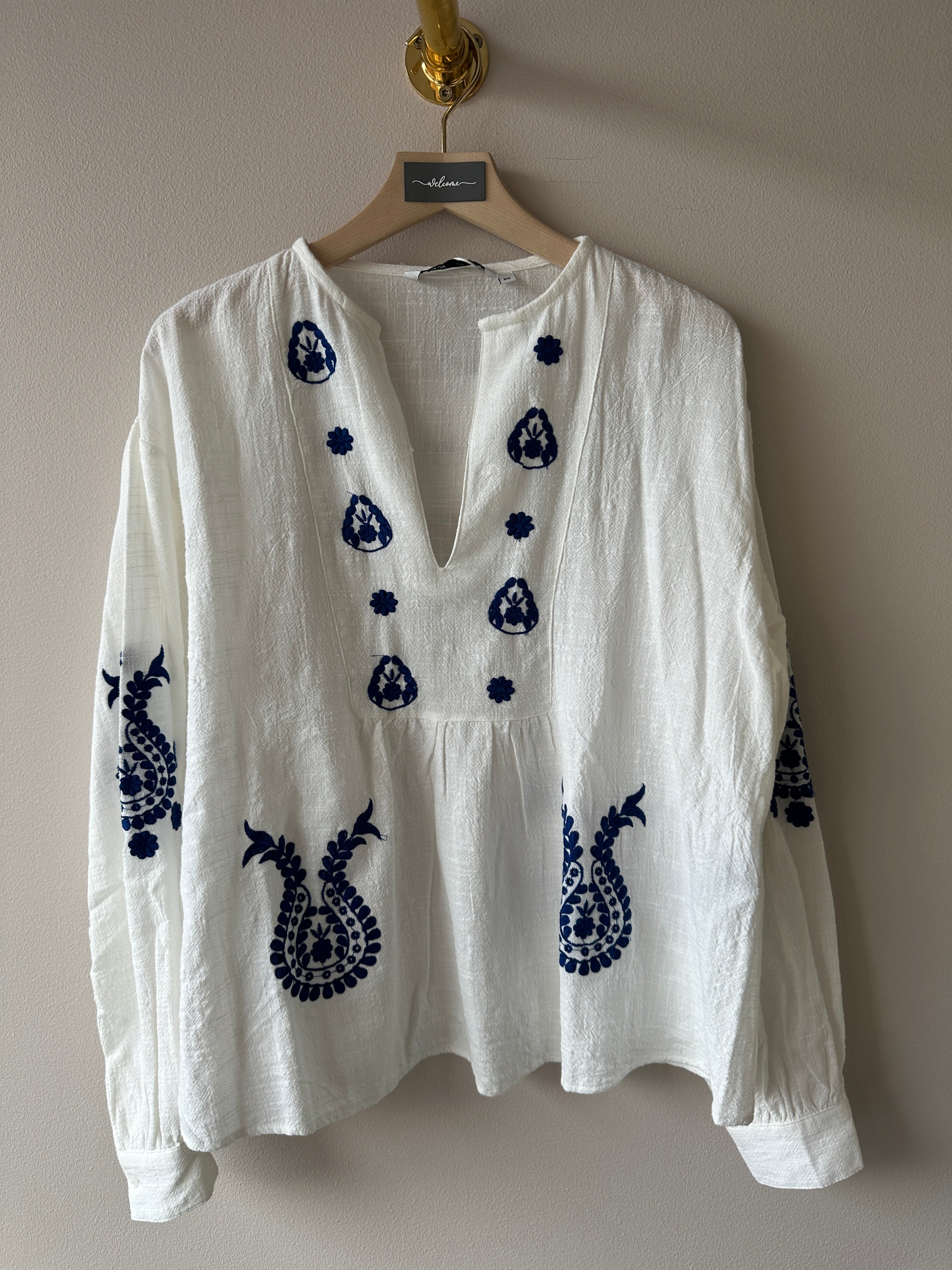 Vit blus med blåa broderi detaljer.