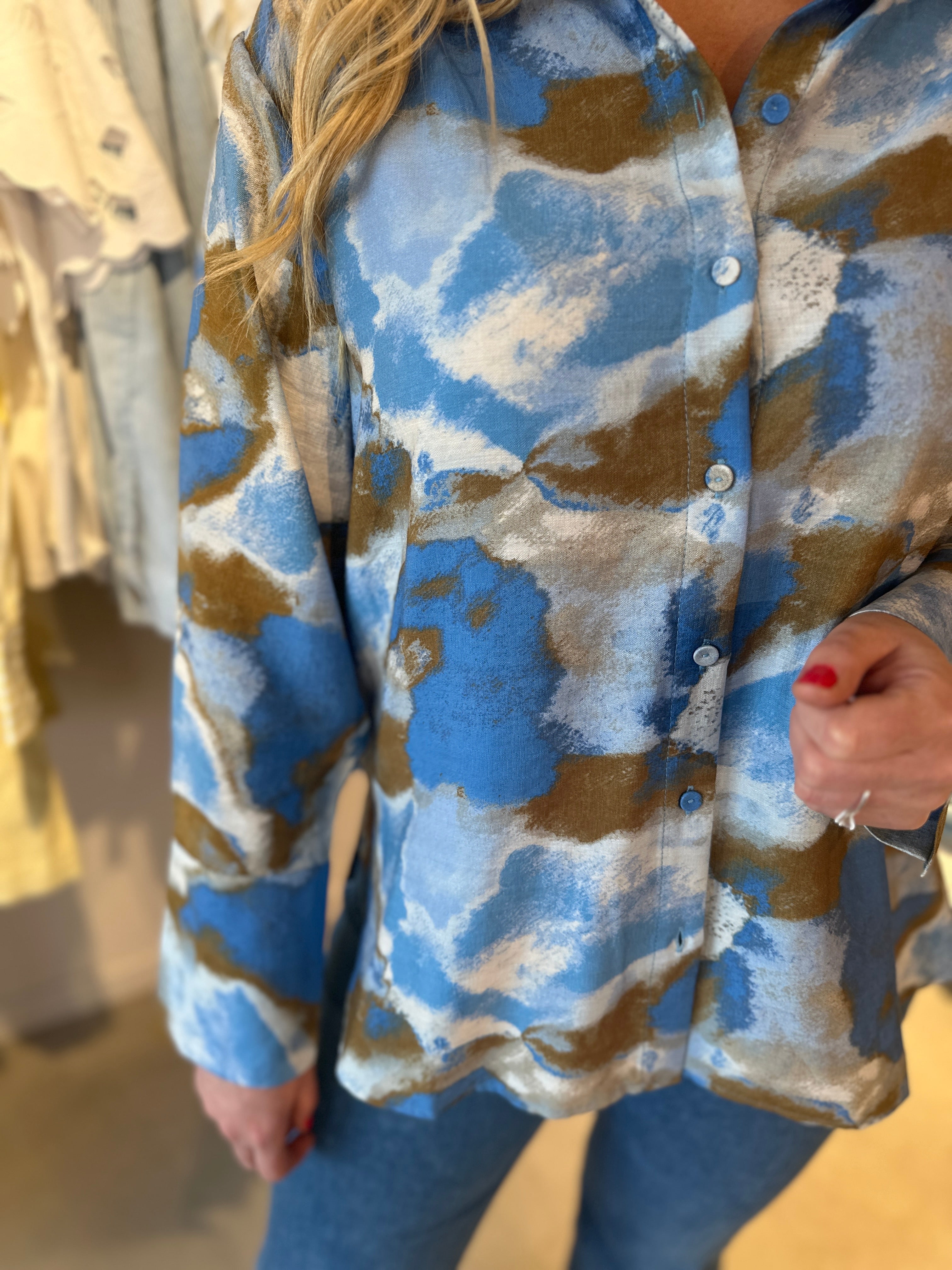 Närbild på överkropp av oversized skjorta med abstrakt blå-khaki-mönster, vita knappar och klassisk krage.