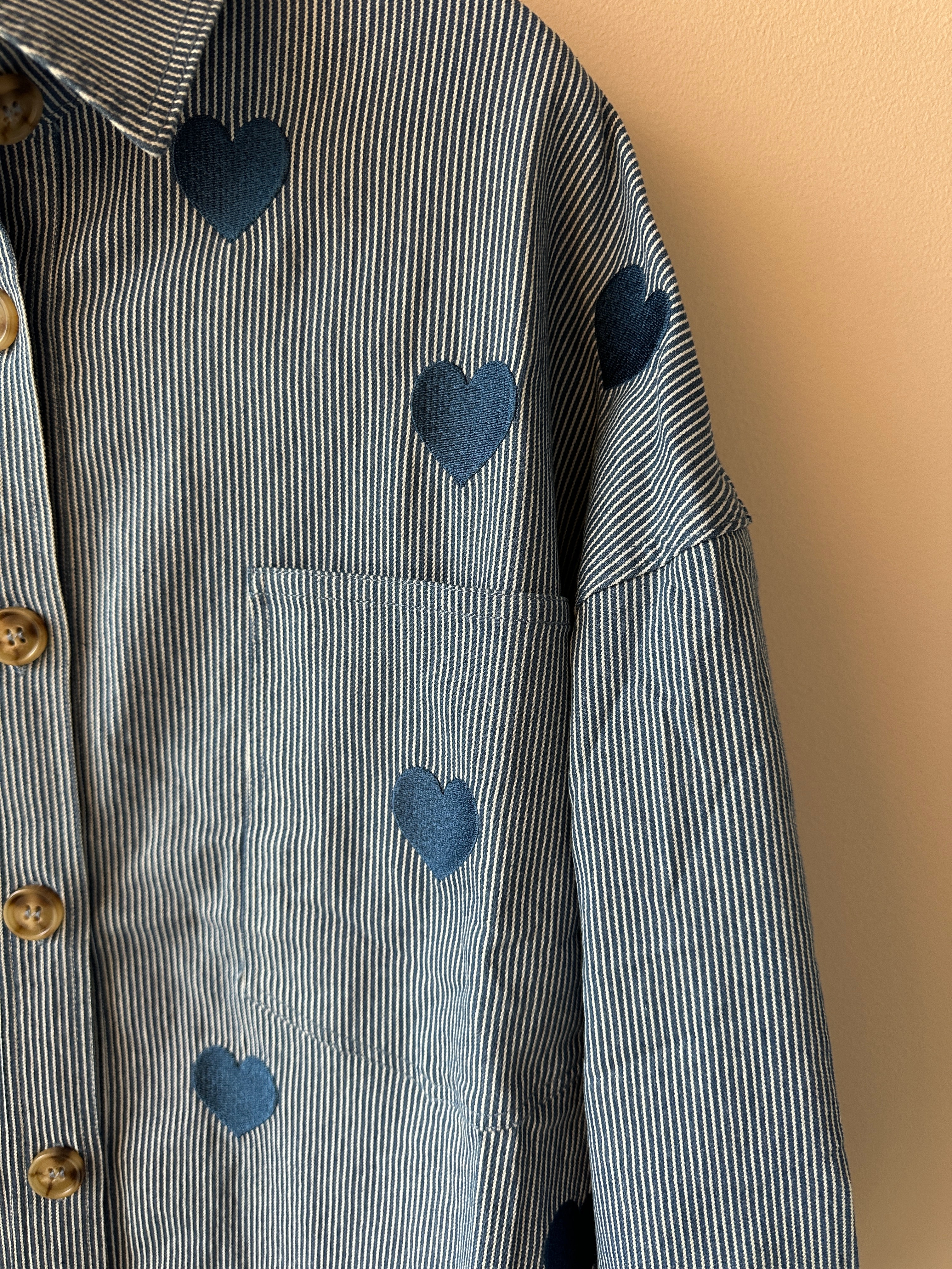 Närbild på broderade hjärtan och guldknappar på blåvitrandig skjortjacka.