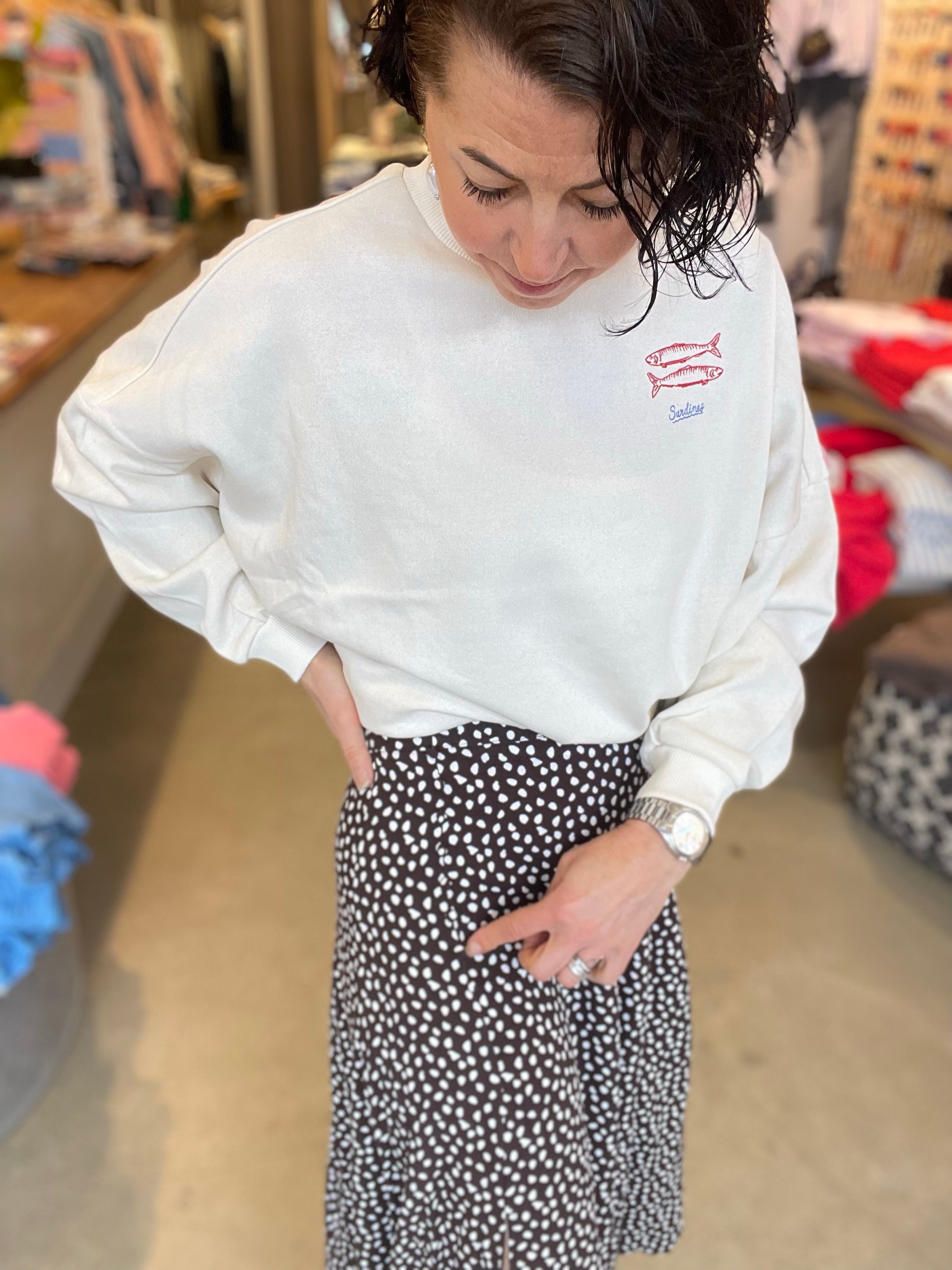 Kvinna i halvprofil med blicken ned i svart prickig midikjol och vit sweatshirt med sardintryck.