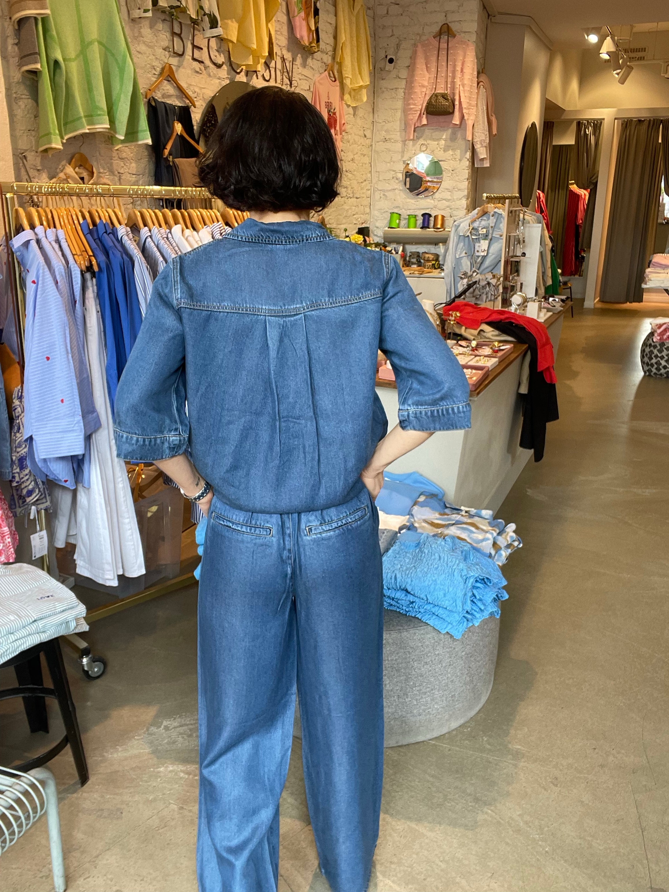 Kvinna bakifrån i vida mellanblå denimbyxor med hög midja och bakfickor, stylade med matchande denimskjorta. 