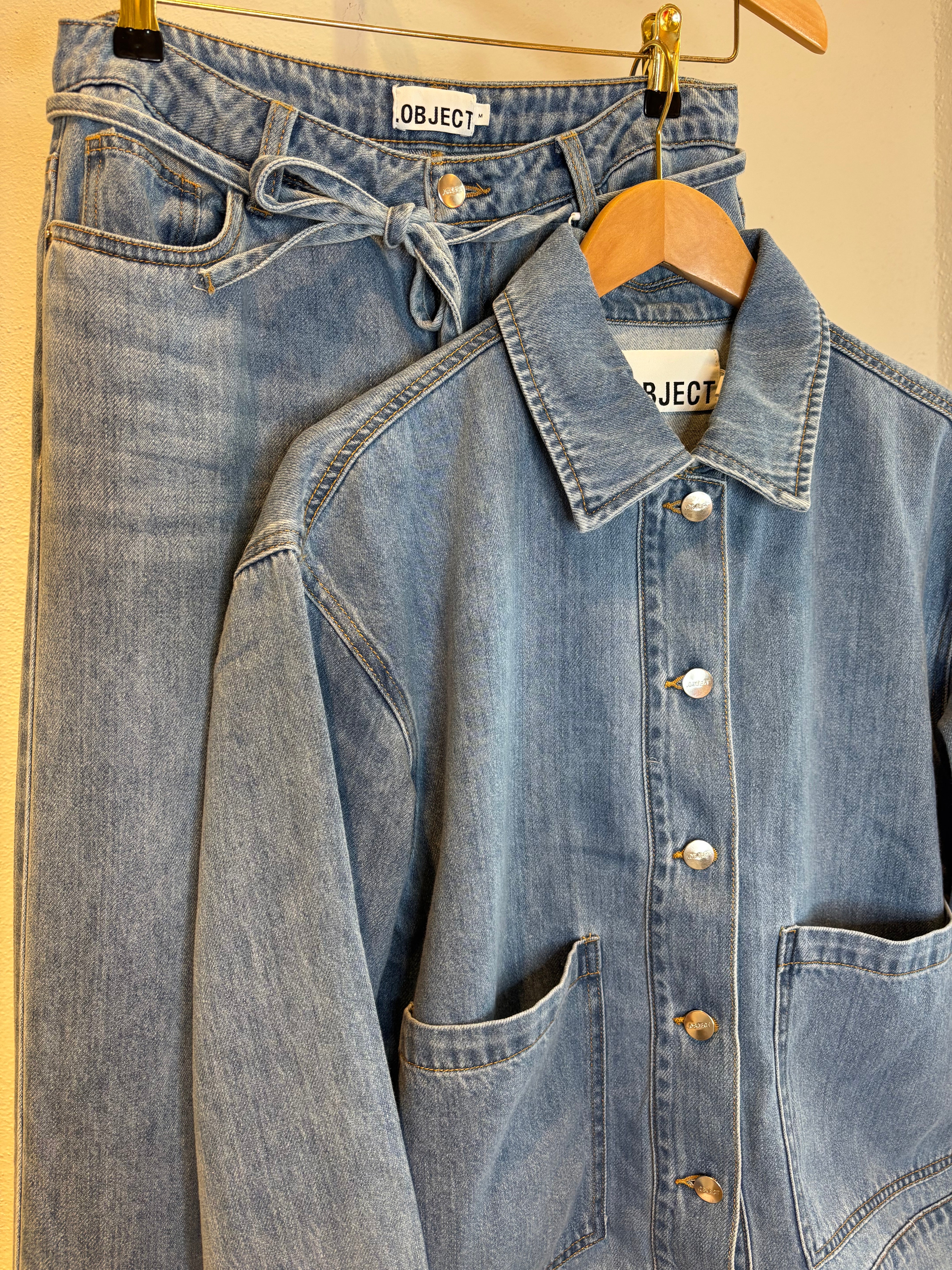 Objrosie Wide Jeans Light Blue Denim. Blåa jeans med snörning hängandes på en galge tillsammans med Objrosie Re Long Sleeve Overshirt Light Blue Denim.