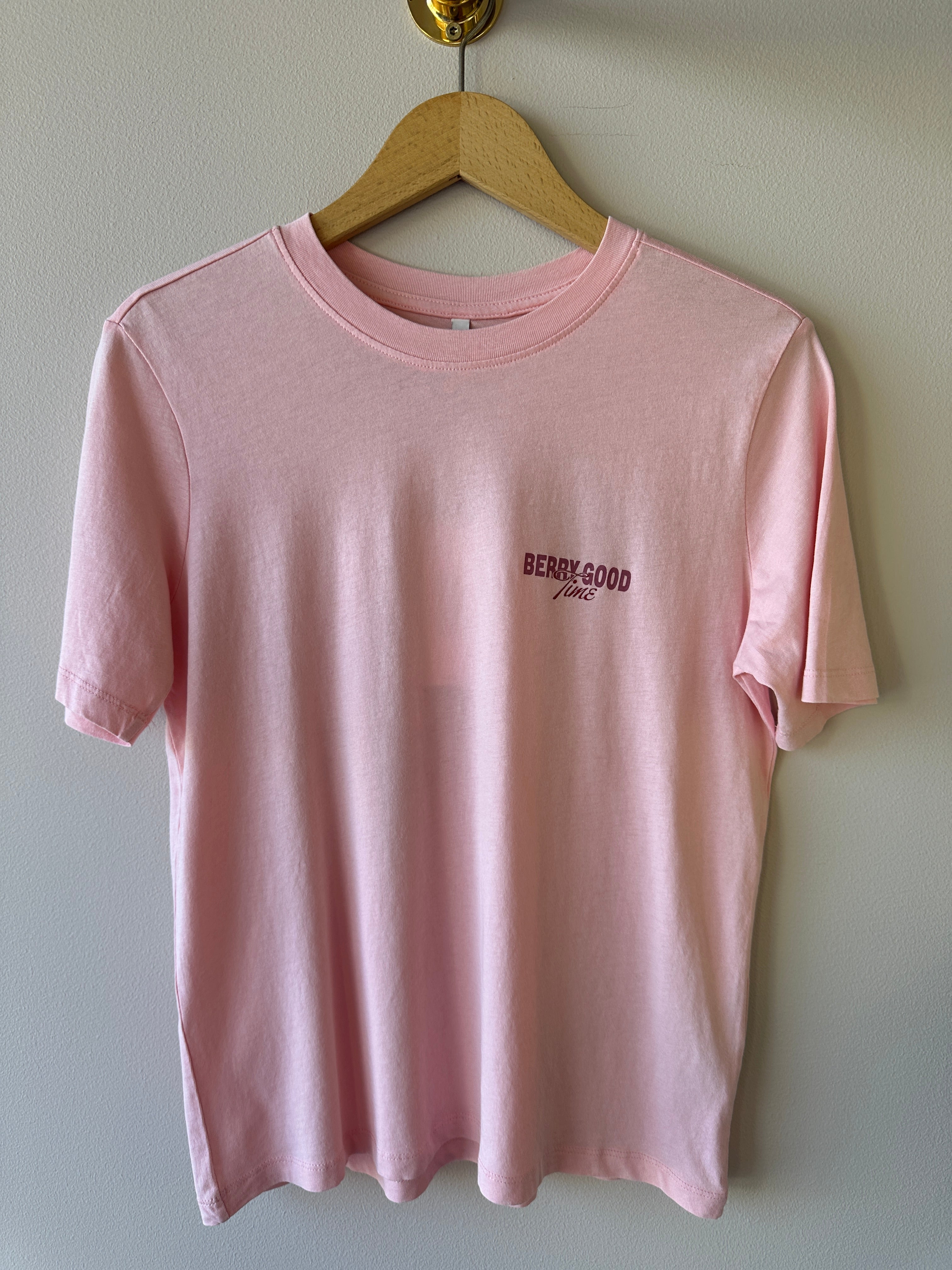 Rosa oversized t-shirt med texten Berry Good Time i mörkrött på bröstet, rund hals och korta ärmar hängande på galge mot beige vägg.