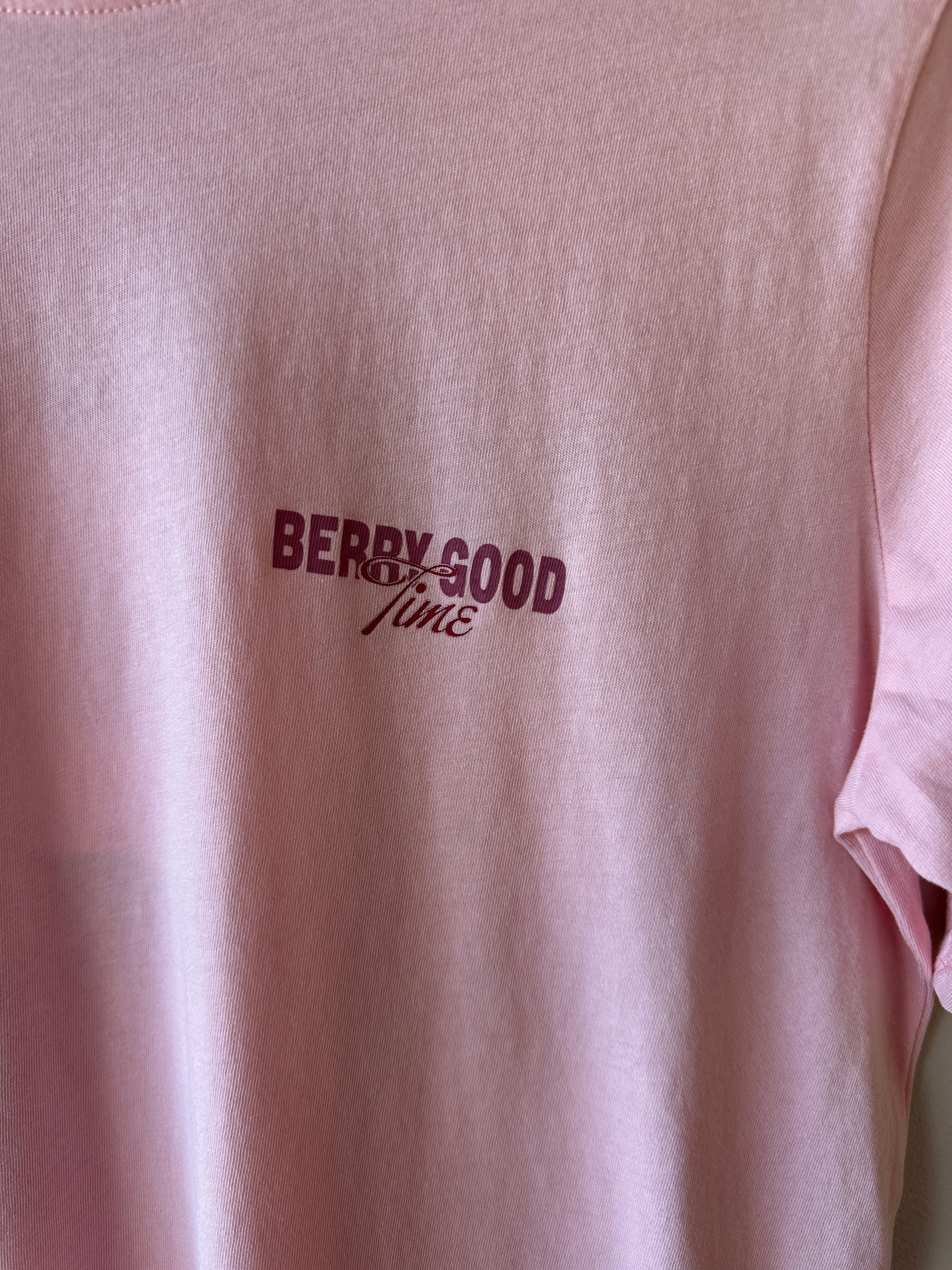 Närbild på bröstet av rosa t-shirt som visar texten Berry Good Time i mörkrött kursiv stil på mjukt rosa bomullstyg.
