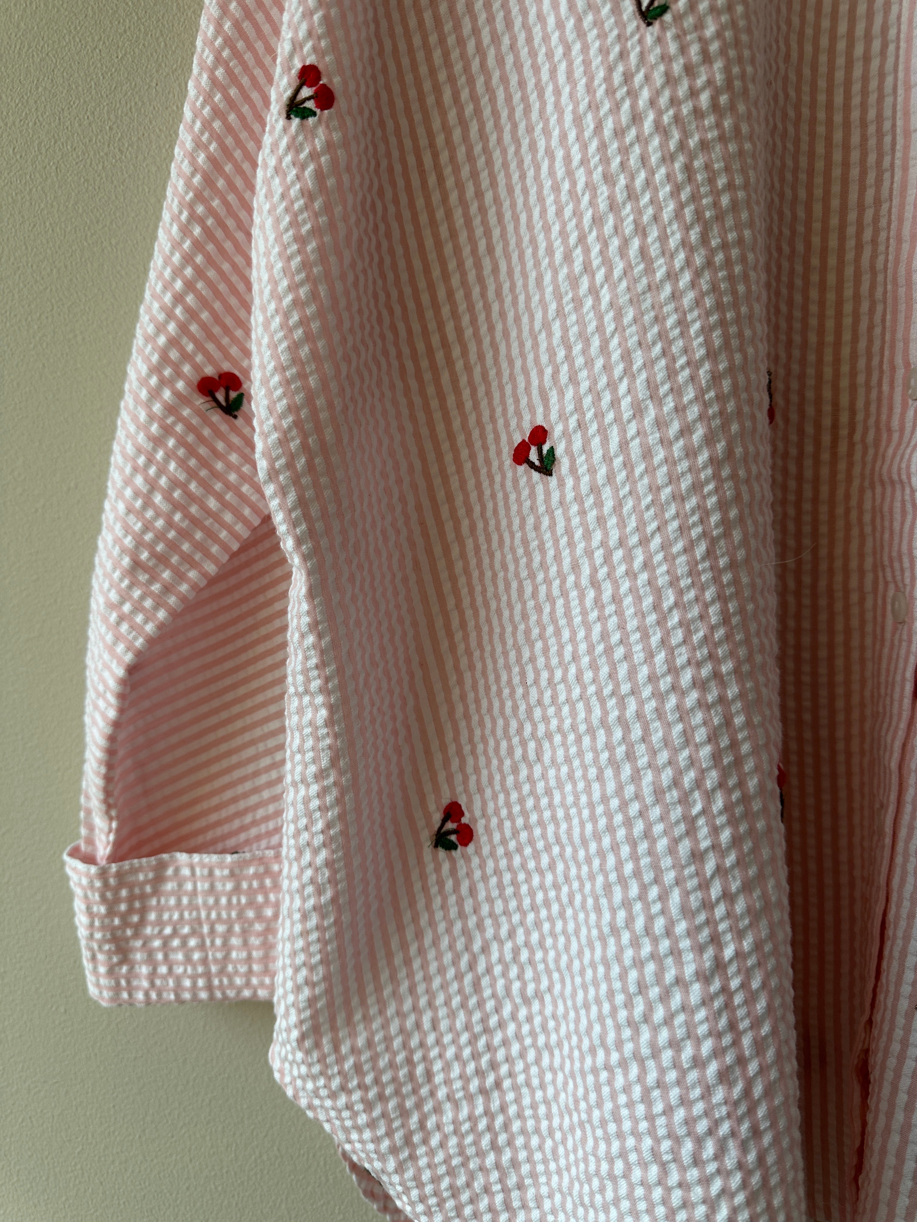 Närbild på ärmslut och krage på vit seersucker-skjorta med broderade körsbär och rosa ränder.