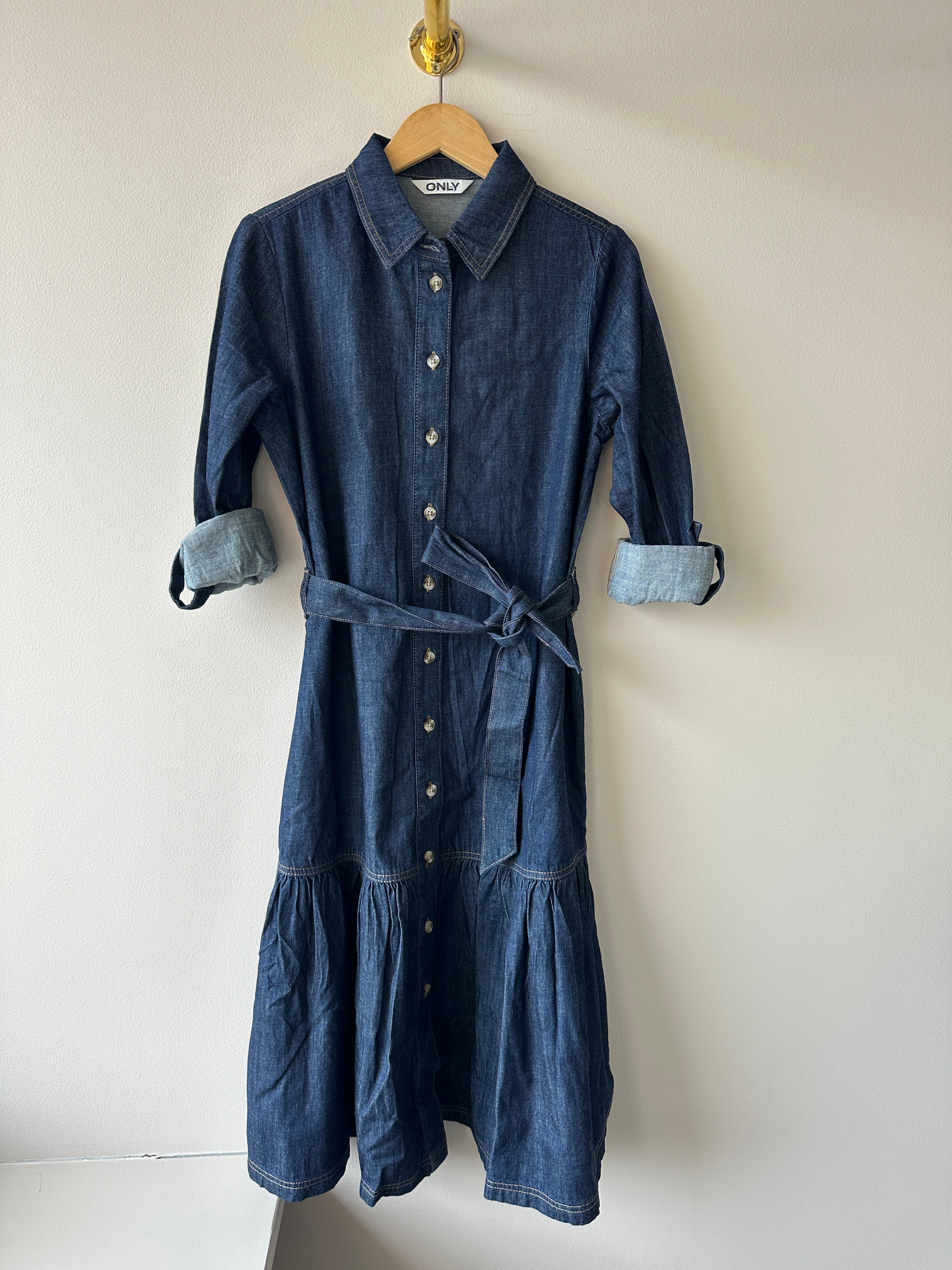 Skjortklänning i jeansmaterial med knäppning framtill med ett skärp. Volang nertill. 