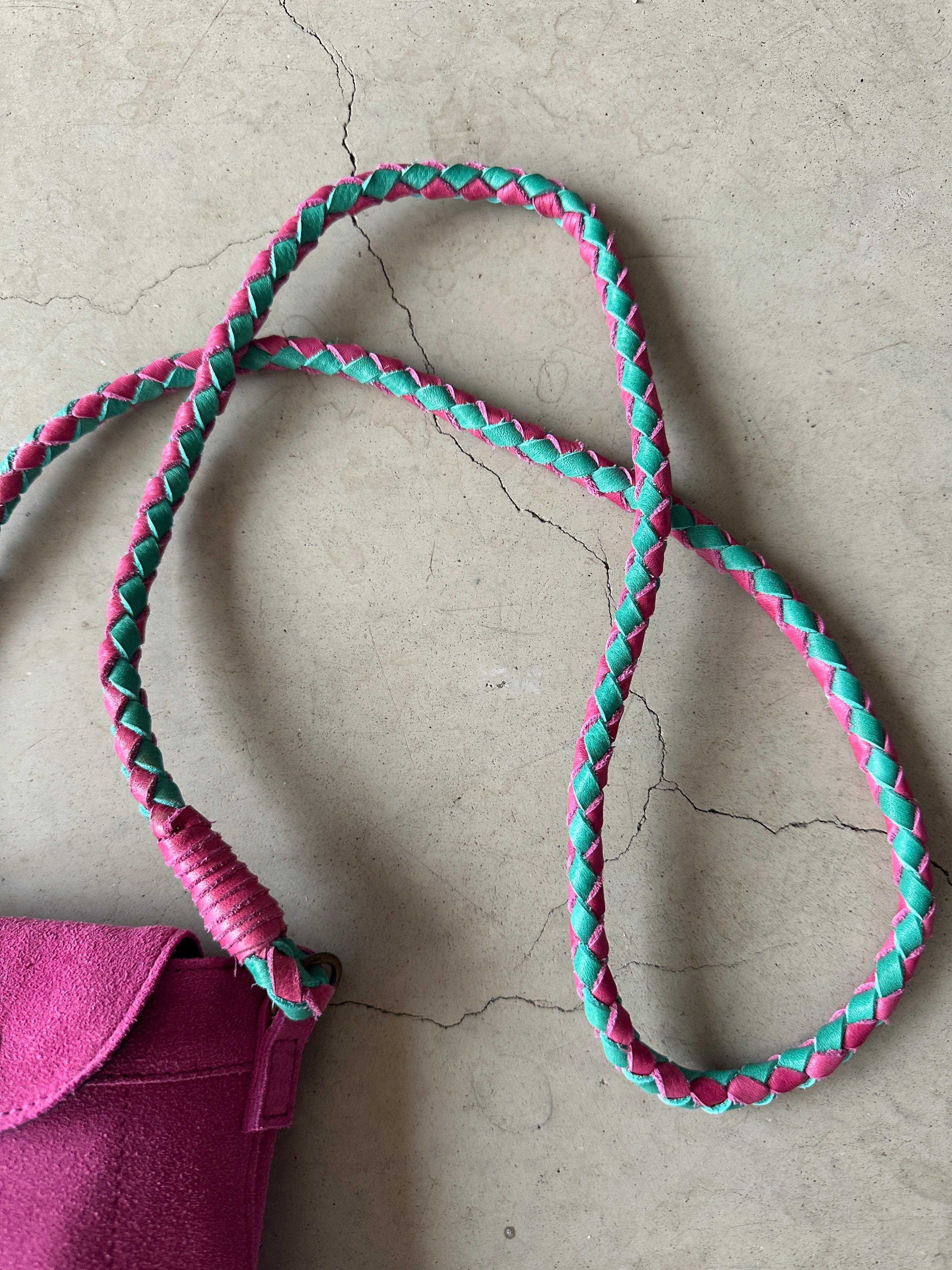 Närbild på flätat axelband i cerise och mintgrönt på fuchsia mocka mobilväska.