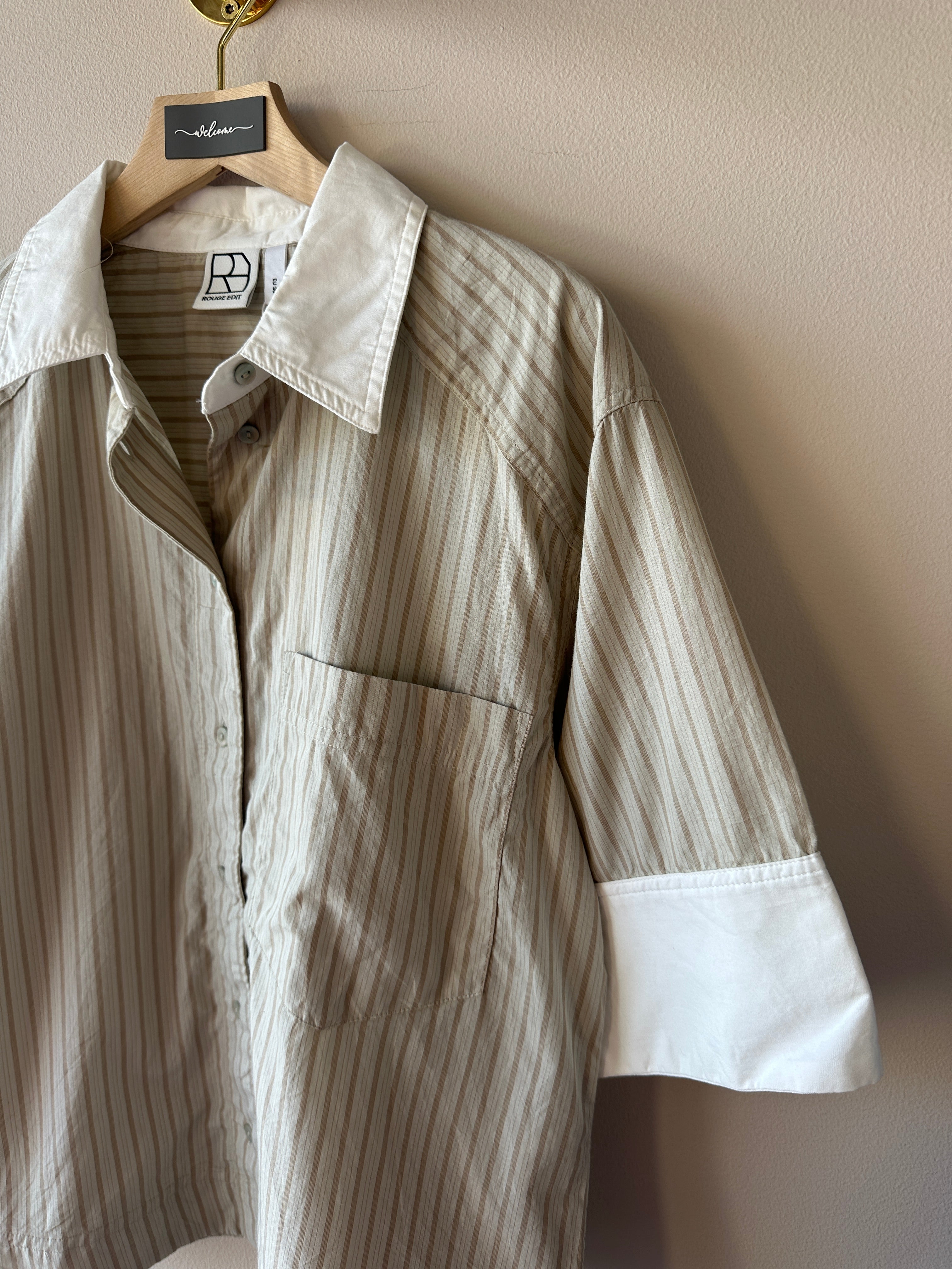 Närbild på beige och vit randig oversized skjorta som visar klassisk krage, brystficka och bred vit manschett på kort ärm, etikett med logotyp Resume synlig.