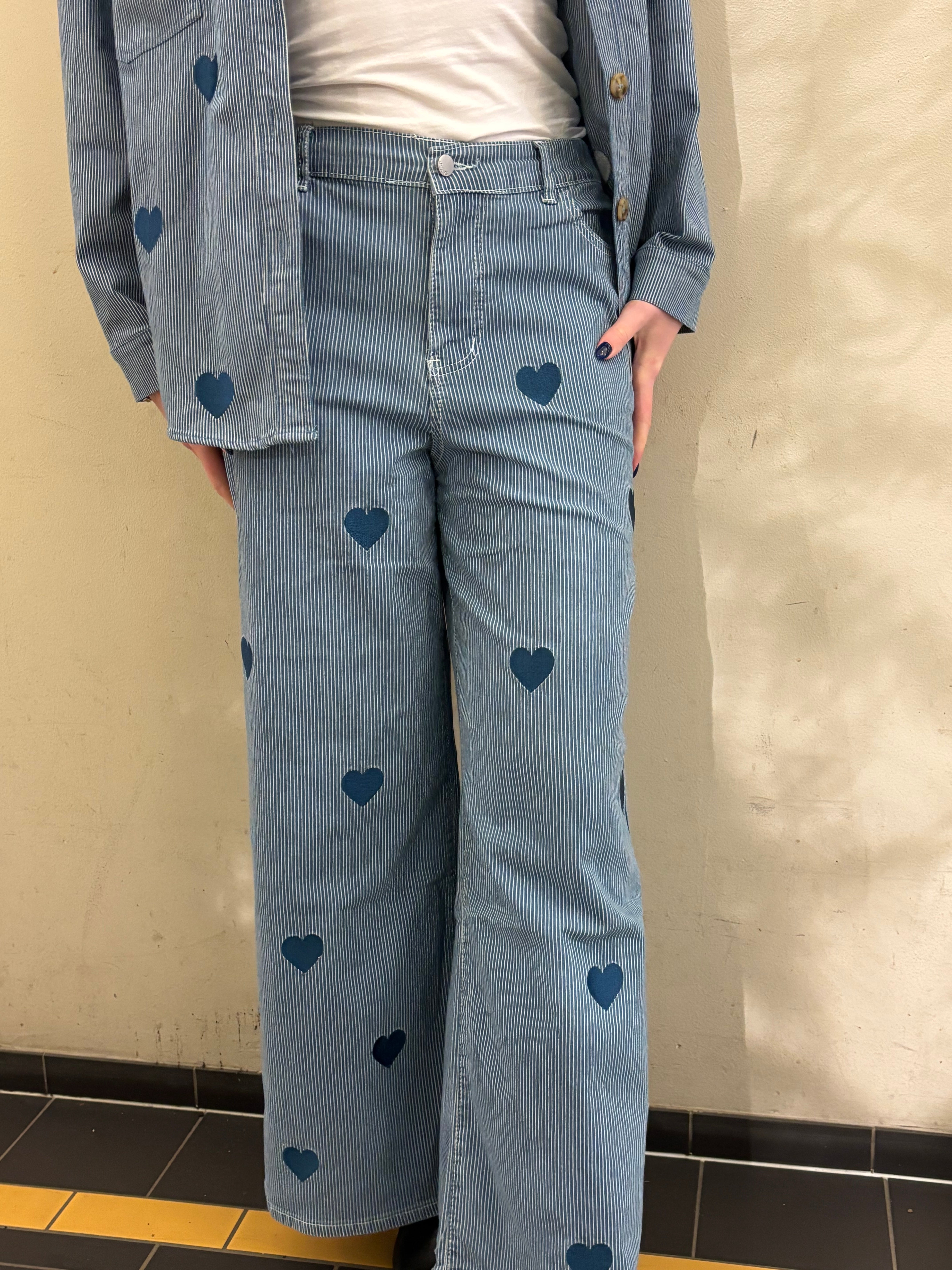 Kvinna i blåvitrandig jeans och matchande skjortjacka med hjärtmönster, helbild.
