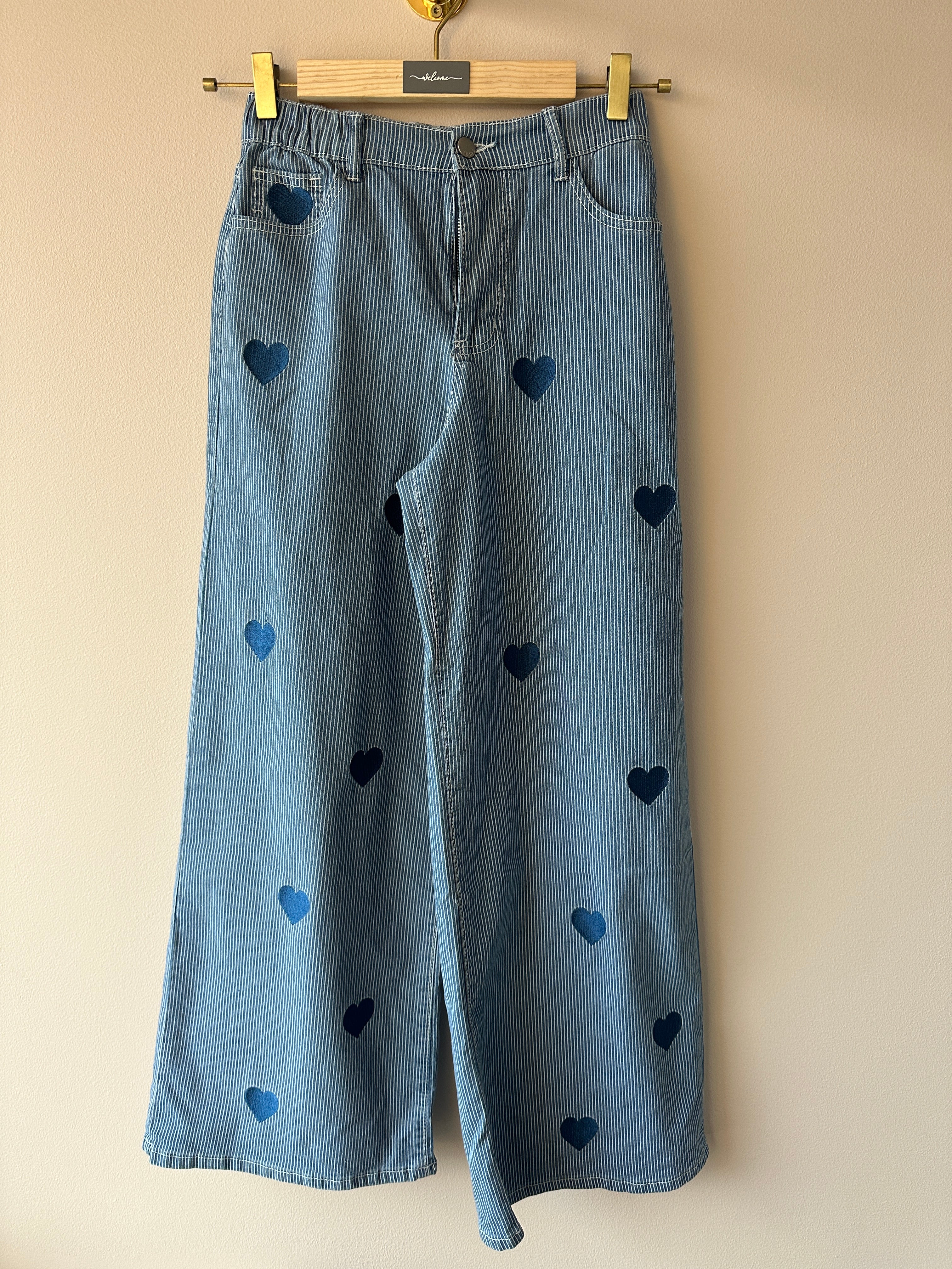 Blåvitrandig jeans med hjärtmönster hängda på galge, helbild framifrån.