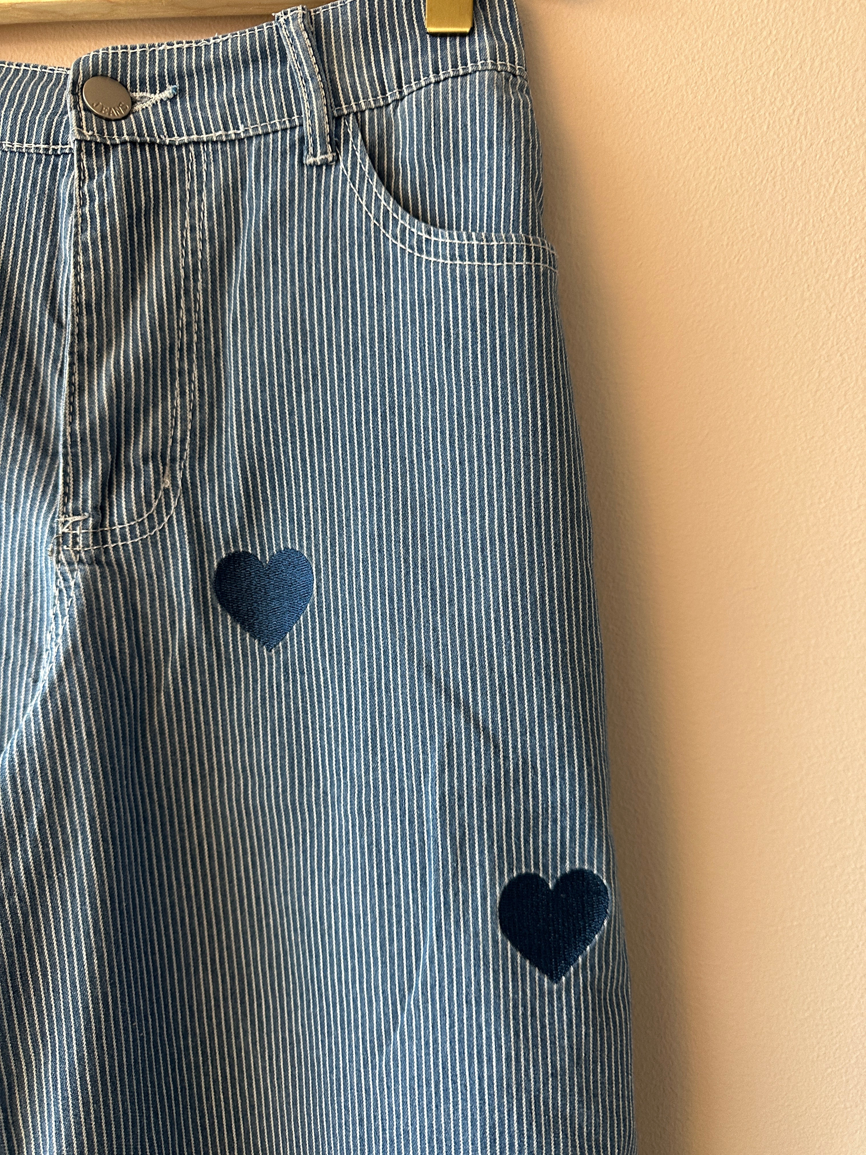 Närbild på broderade hjärtan på blåvitrandig jeans, hängda på galge.