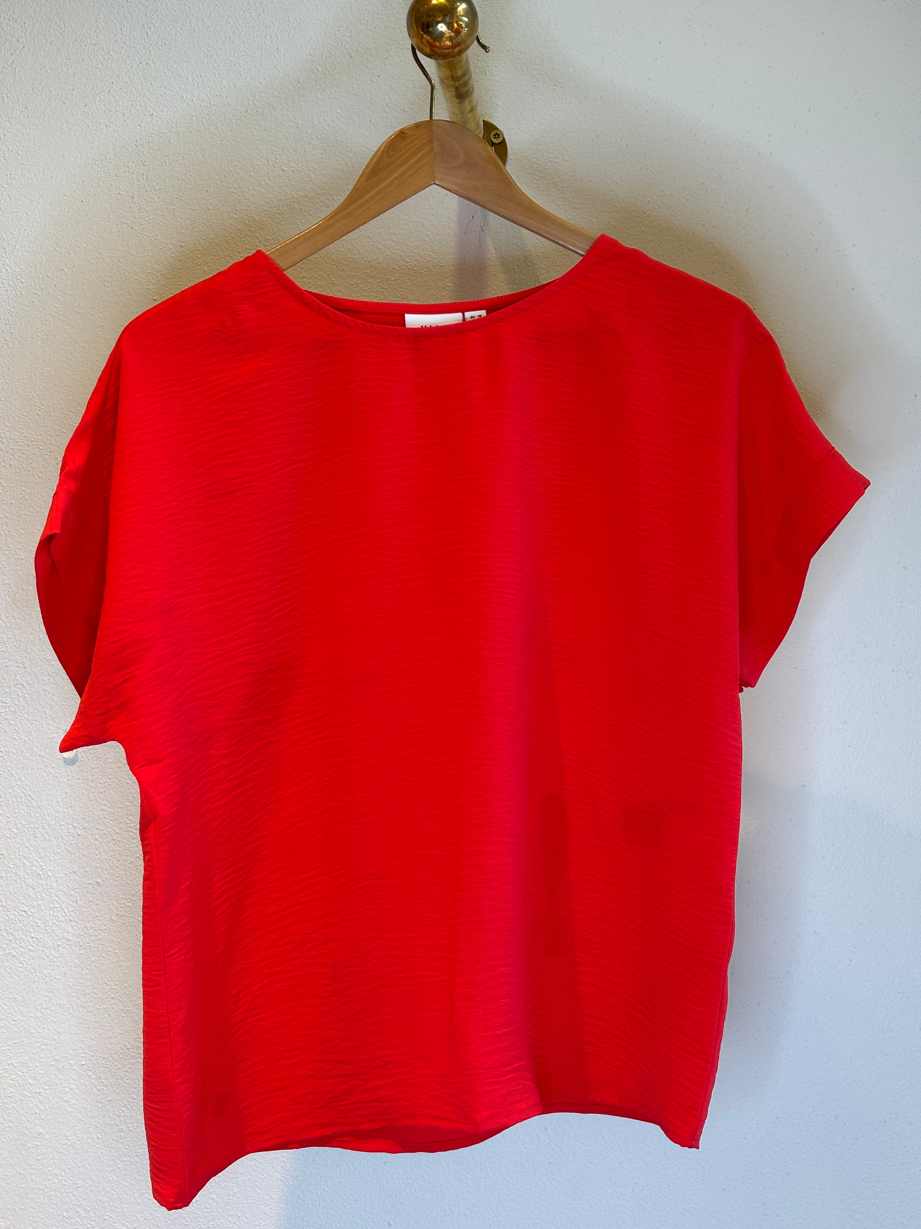 Vijosa Short Sleeve Top Hibiscus. Röd kortärmad blus hängandes på en galge.