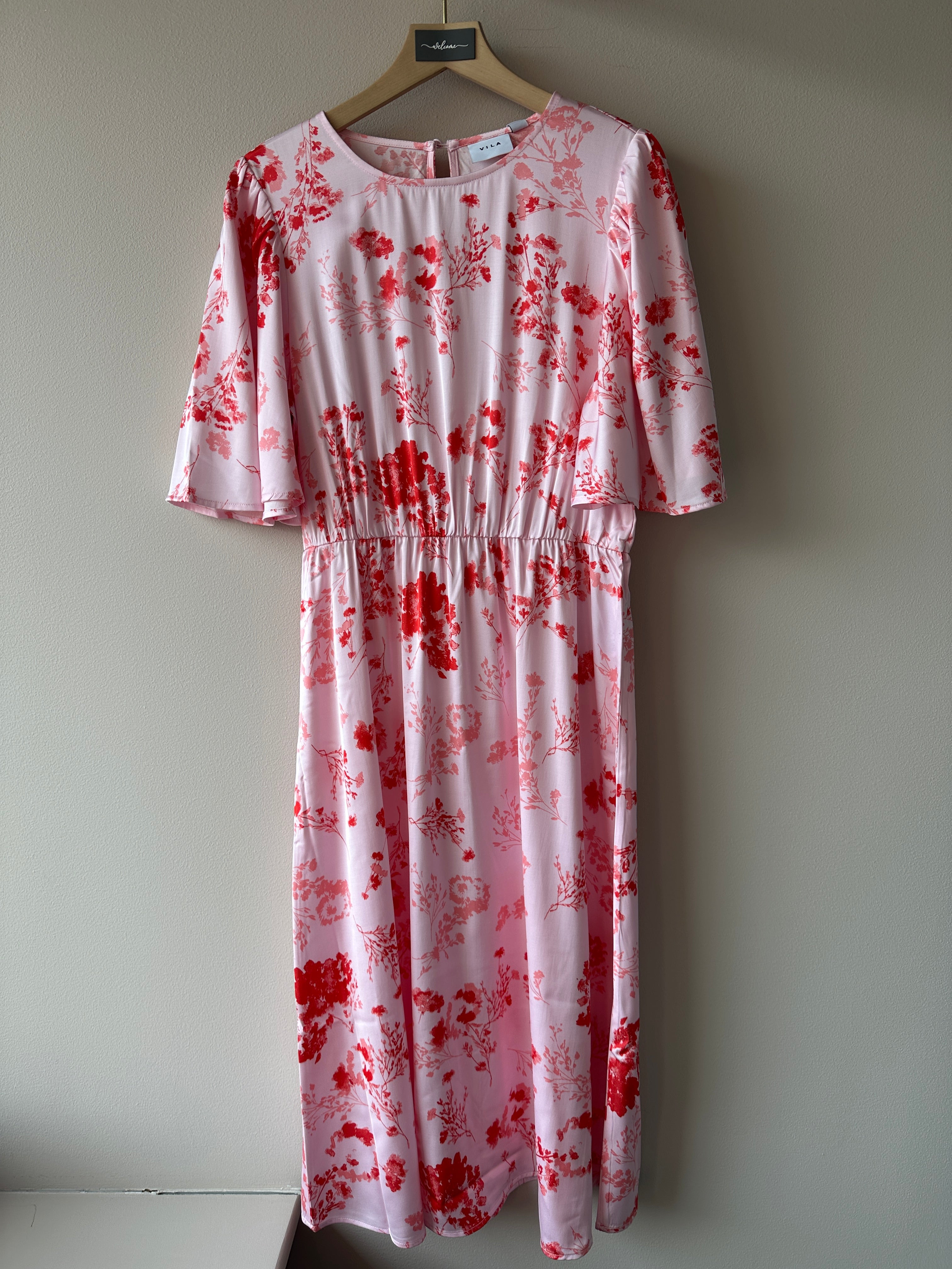 Vithalia Anya O Neck Dress Cherry Blossom Anya. Rosa röd blommig klänning, hängandes på en galge.