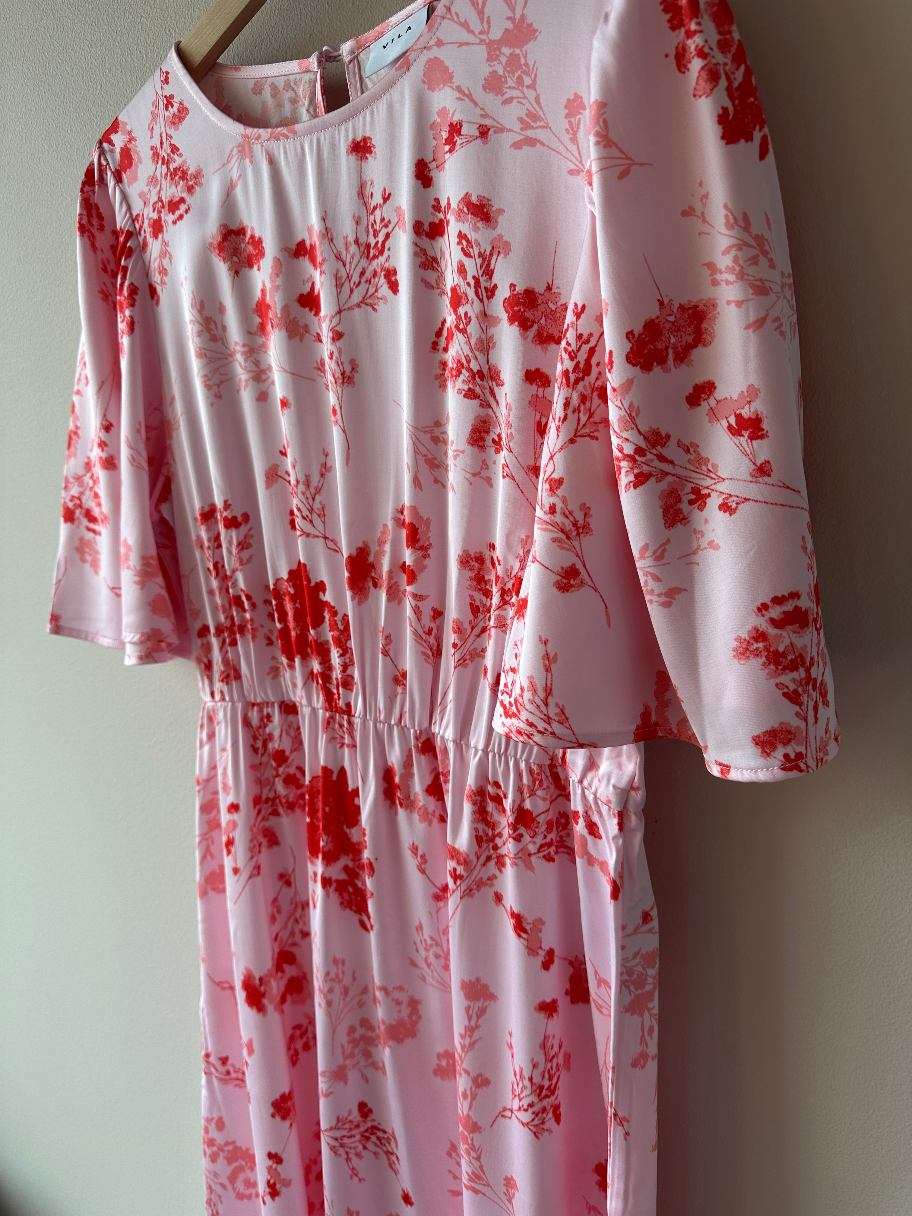 Vithalia Anya O Neck Dress Cherry Blossom Anya. Rosa röd blommig klänning, hängandes på en galge.